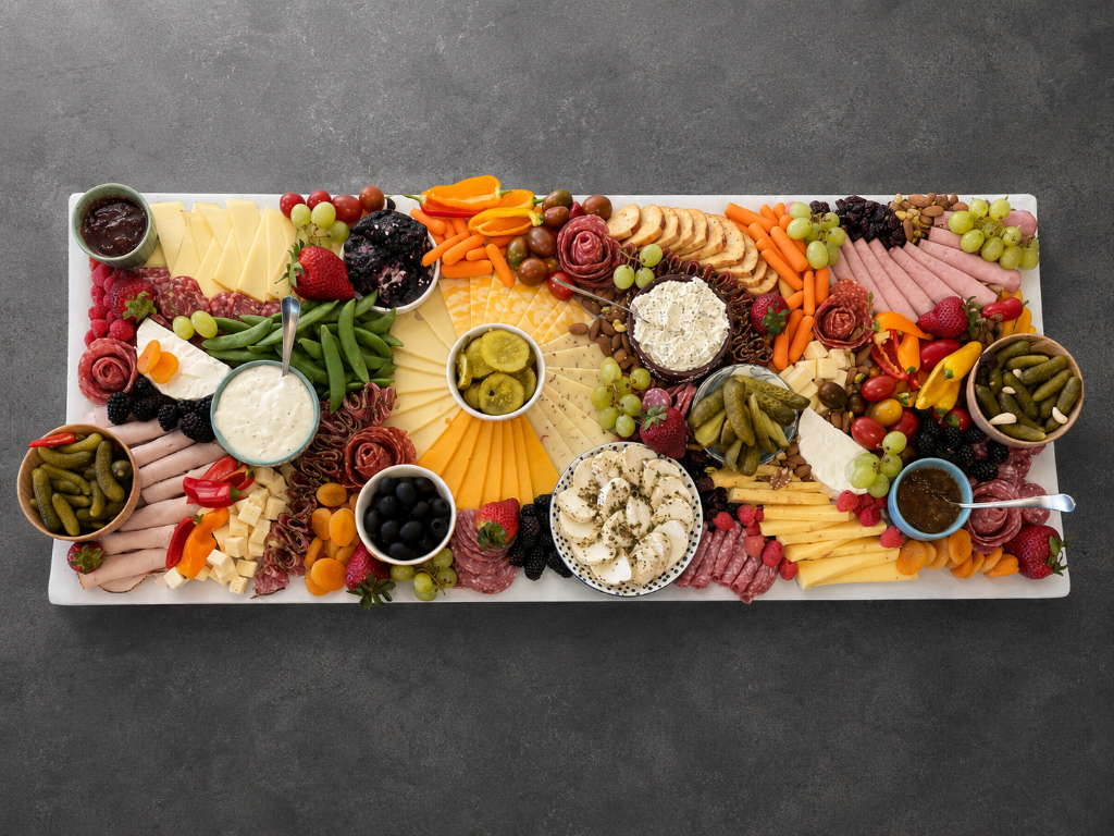 A rectangular grazing board with cheeses, cured meats, pickles, mozzarella, and fresh fruit